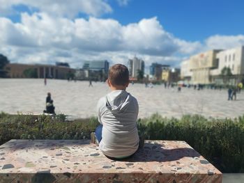 Rear view of boy in city against sky