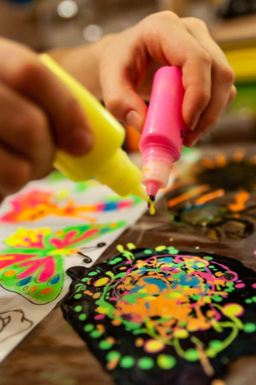 CLOSE-UP OF PERSON HAND HOLDING MULTI COLORED PAPER