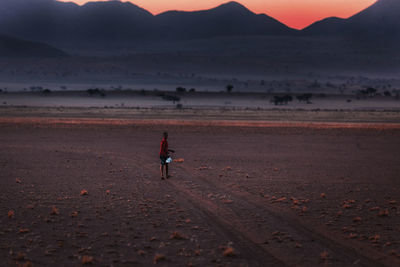 Full length of man walking on land against sky during sunset