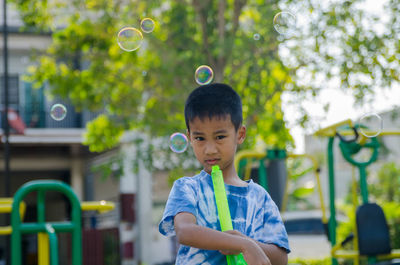 Portrait of boy playing with bubbles against trees