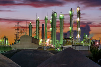 Panoramic view of illuminated factory against sky at sunset