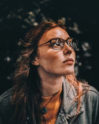 Close-up of young woman with eyeglasses against black background