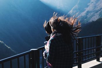 Female friends with tousled hair standing by railing against mountains