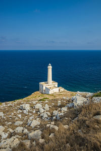 Lighthouse by sea against clear blue sky