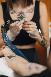 Female tattoo artist prepares tattoo machine for making a tattoo on a mens arm