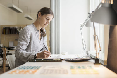 Serious woman painting while sitting at table in creative office