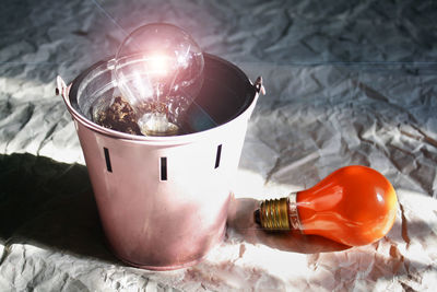 High angle view of illuminated light bulb in bucket on crumpled paper