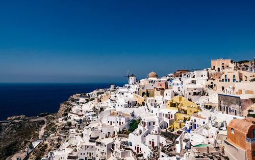 High angle view of townscape by sea against clear blue sky