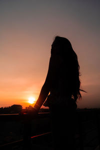 Rear view of silhouette woman standing against orange sky