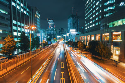 Light trails on road amidst buildings against sky at night