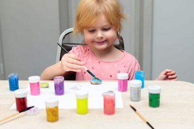 Little smiling child painting pebbles with colorful paints on the table.
