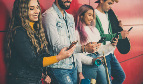 Friends using smart phones while standing against wall