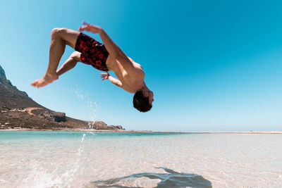 Man jumping over sea against clear blue sky