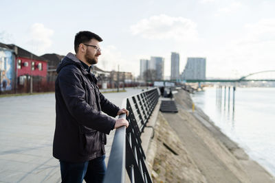 Man standing on railing in city against sky