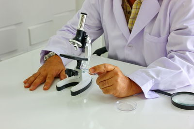 Midsection of scientist with microscope on table sitting in laboratory