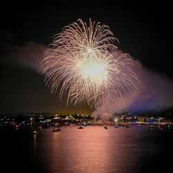 Firework display over illuminated city against sky at night