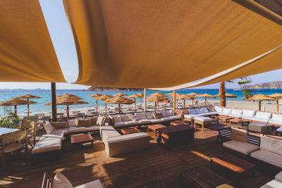 Empty chairs and tables in restaurant by sea against sky