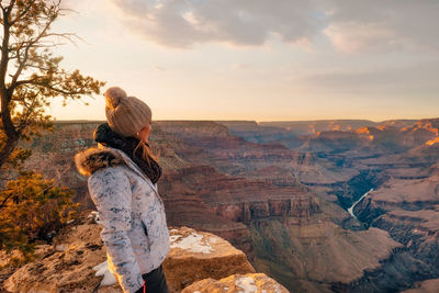 Rear view of woman standing on rock against sky