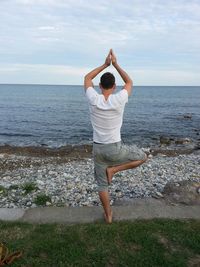Rear view of man doing yoga at beach against sky