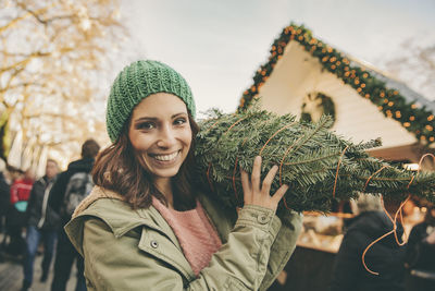 Happy woman with a wrapped-up tree walking over the christmas market