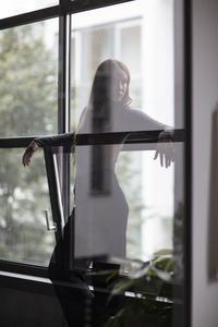 Thoughtful young woman standing by windows