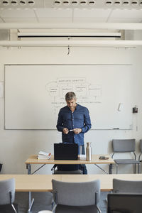 Male professor looking at laptop on desk in classroom