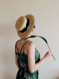 Rear view of woman holding hat standing against white background
