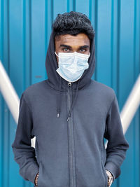 Portrait of young man wearing mask standing against wall