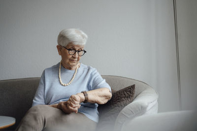 Senior woman checking time on wristwatch sitting at home