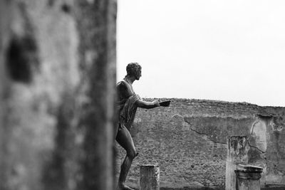 Side view of man standing on wall against sky