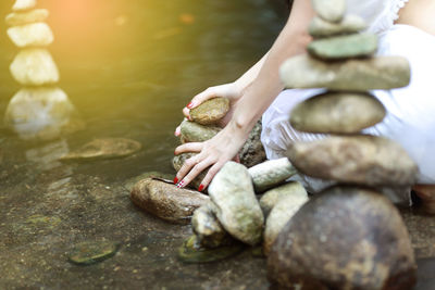 Midsection of woman sitting by stones by lake