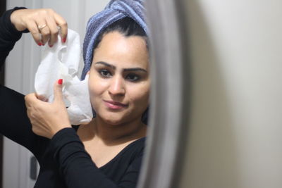 Woman removing facial mask reflecting in mirror