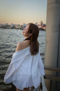 Side view of young woman standing against sea