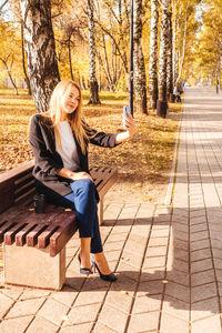 Full length of woman drinking coffee while talking over phone on bench