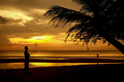 Silhouette people standing on beach during sunset