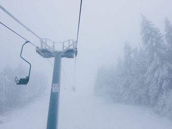 Overhead cable car on snow covered landscape in foggy weather