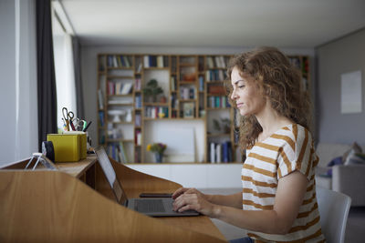 Woman using phone while sitting on table at home