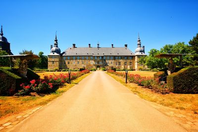 Road passing through buildings against blue sky