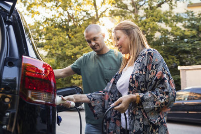 Mature couple charging black electric car in back yard