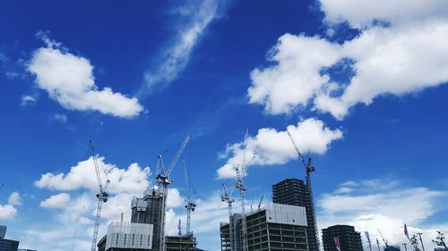 Low angle view of buildings and cranes against cloudy sky