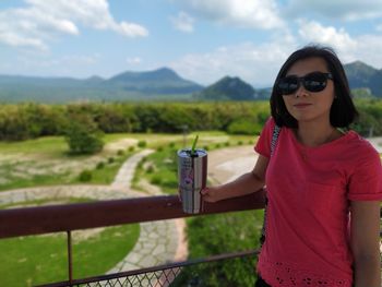 Woman wearing sunglasses standing by railing against mountains