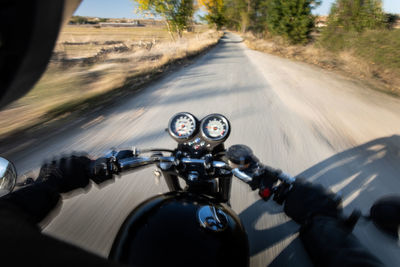 Back view of faceless fast racer riding motorbike through forest in rural location