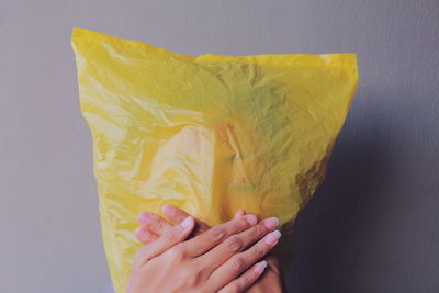 Woman covering face with yellow plastic bag against wall