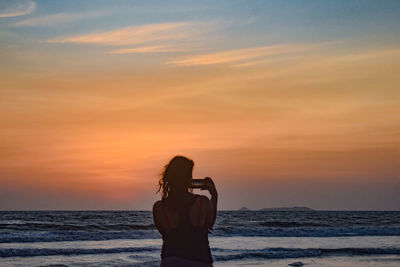 Rear view of woman standing on beach during sunset