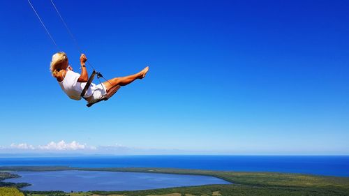 Man jumping over sea against clear blue sky