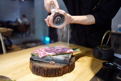 Midsection of man sprinkling salt on raw meat at kitchen