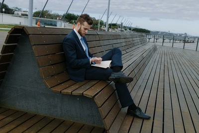 Young businessman reading book while sitting on bench