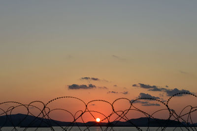 Silhouette fence against sky during sunset