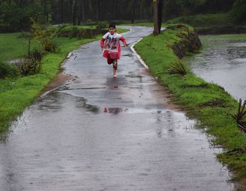 Full length of boy walking on wet road during rainy season