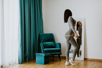 Full length of woman standing on chair at home